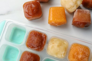 Different fruit puree in ice cube tray on white table, flat lay