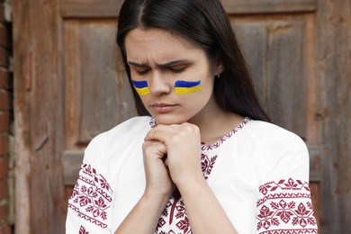 Photo of Sad young woman with drawings of Ukrainian flag on face near wooden door