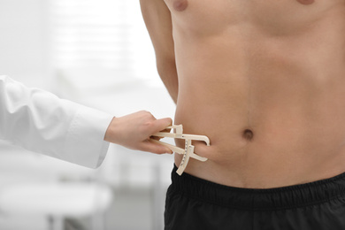 Nutritionist measuring man's body fat layer with caliper on blurred background, closeup