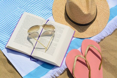 Beach towel with book, straw hat, sunglasses and flip flops on sand
