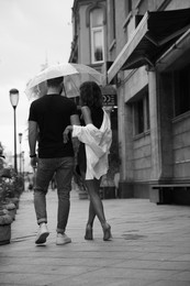 Image of Young couple with umbrella enjoying time together under rain on city street, back view. Black and white effect