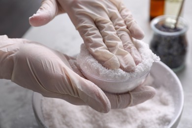 Photo of Woman in gloves making bath bomb at grey table, closeup