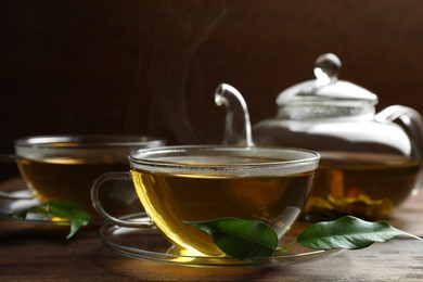 Photo of Fresh green tea in glass cups, leaves and teapot on wooden table, closeup
