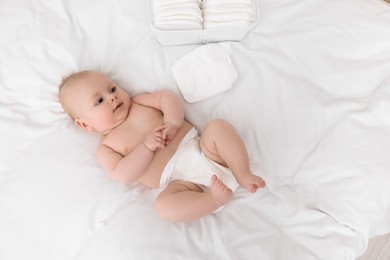 Photo of Cute baby and diapers on white bed, top view