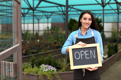 Photo of Female business owner holding OPEN sign in greenhouse. Space for text