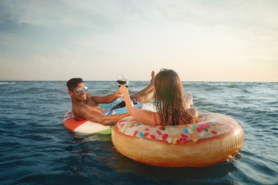 Couple with glasses of wine and inflatable rings in sea