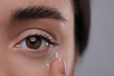 Closeup view of young woman putting in contact lens on grey background