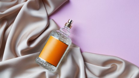 Photo of Luxurious bottle of perfume and beige silk on pink background, top view. Space for text