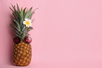 Photo of Funny pineapple with sunglasses and plumeria flower on pink background, space for text. Creative concept