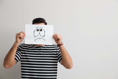 Man hiding emotions using card with drawn frowning face on white background
