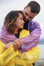 Young couple in raincoats enjoying time together under rain on beach