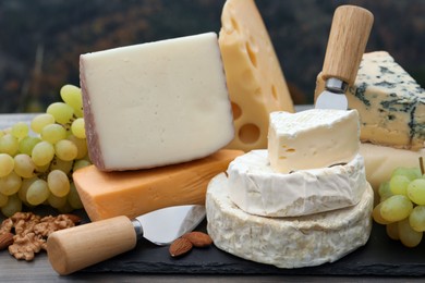 Different types of delicious cheeses and snacks on wooden table outdoors