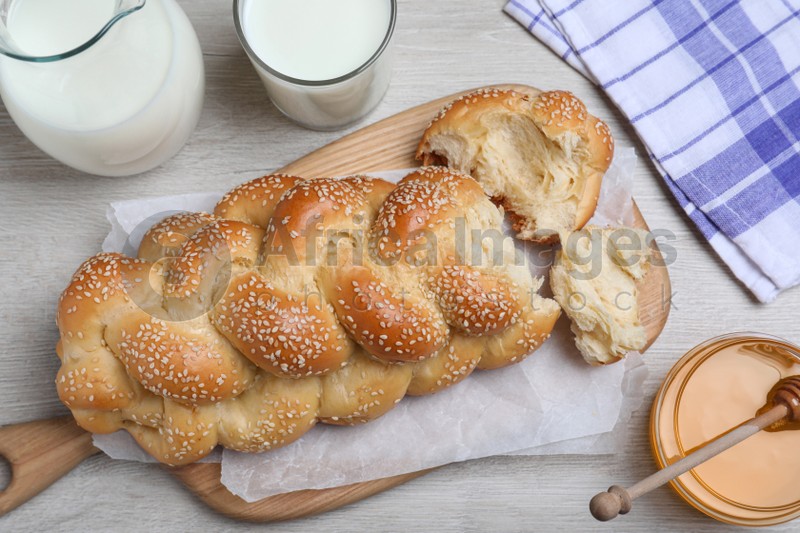 Broken homemade braided bread, milk and honey on white wooden table, flat lay. Traditional Shabbat challah