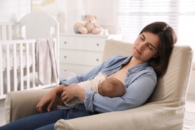 Tired young mother sleeping while breastfeeding her baby in children's room