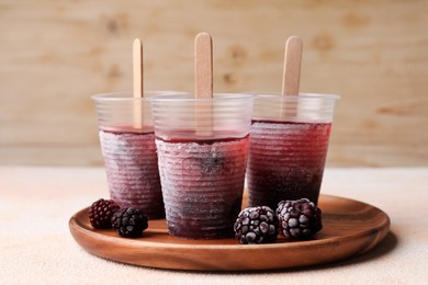 Tasty blackberry ice pops in plastic cups on white table. Fruit popsicle