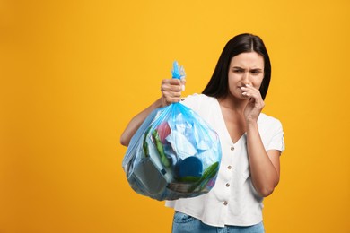 Woman holding full garbage bag on yellow background. Space for text