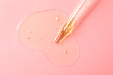 Dripping hydrophilic oil from pipette on pink background, top view
