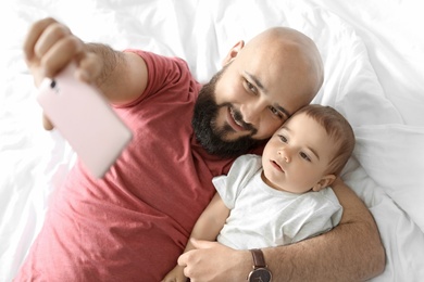 Dad taking selfie with his little son on bed