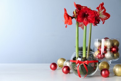 Photo of Beautiful red amaryllis flowers and Christmas decor on white table. Space for text