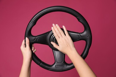 Woman holding steering wheel on crimson background, closeup