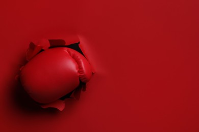 Man breaking through red paper with boxing glove, closeup. Space for text