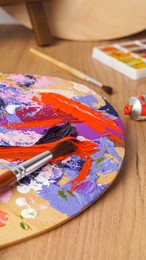 Photo of Artist's palette with mixed paints and brushes on wooden table, closeup