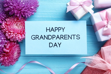 Beautiful flowers, gift boxes and card with phrase Happy Grandparents Day on light blue wooden background, flat lay