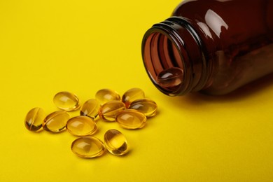 Photo of Overturned bottle with dietary supplement capsules on yellow background, closeup