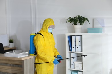 Employee in protective suit sanitizing office. Medical disinfection