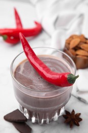 Photo of Glass of hot chocolate with chili pepper on white marble table, closeup