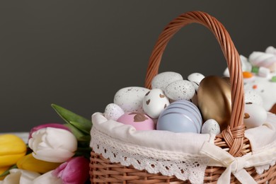 Photo of Wicker basket with festively decorated Easter eggs and beautiful tulips on dark grey background, closeup