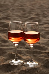 Photo of Glasses of tasty rose wine on sand