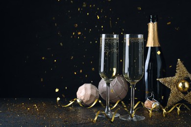 Happy New Year! Bottle of sparkling wine, glasses and festive decor on black background, space for text