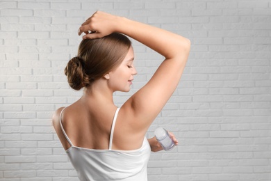 Young woman applying crystal alum deodorant to armpit against brick wall