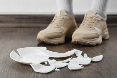 Woman in sneakers standing near broken plate on floor indoors, closeup