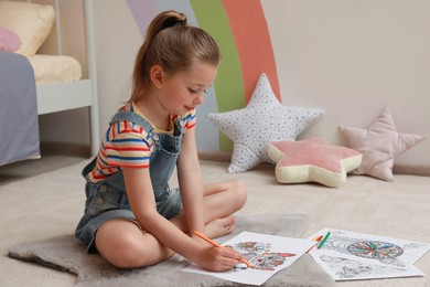 Little girl coloring antistress page on floor indoors