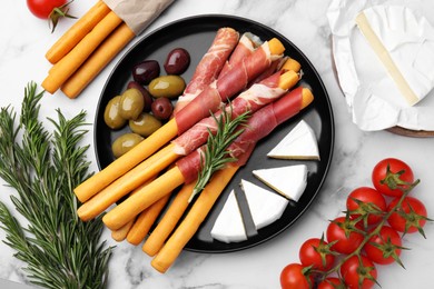 Photo of Delicious grissini sticks with prosciutto and ingredients on white marble table, flat lay