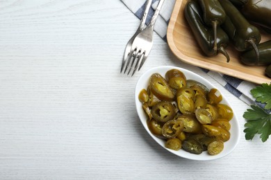 Photo of Bowl with slices of pickled green jalapeno peppers on white wooden table, flat lay. Space for text