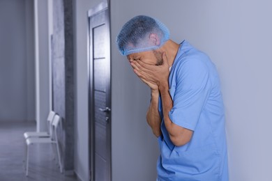 Crying doctor near grey wall in hospital, space for text