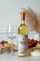 Bottle of white wine, glass and snacks on table
