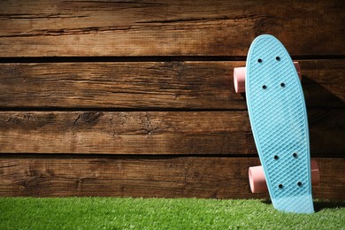 Photo of Light blue skateboard with pink wheels on green grass near wooden wall, space for text