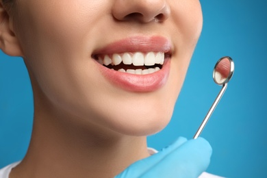 Doctor examining woman's teeth on blue background, closeup. Cosmetic dentistry