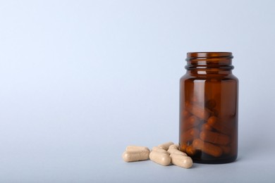 Gelatin capsules and bottle on light grey background, space for text