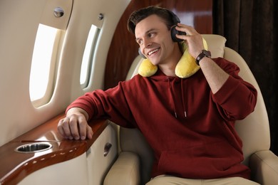 Young man with travel pillow and headphones listening to music in airplane during flight