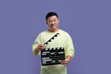 Photo of Happy asian actor with clapperboard on purple background. Film industry