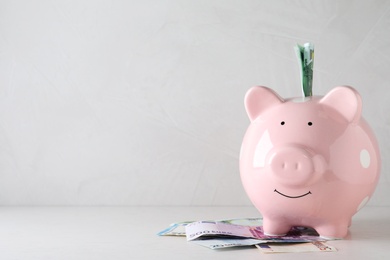 Pink piggy bank with money on light table, space for text
