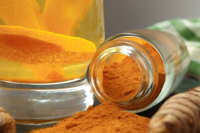 Photo of Glass cup of tasty tea, turmeric roots and powder on table, closeup