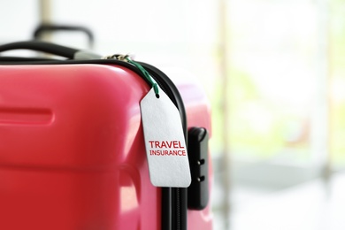Stylish suitcase with travel insurance label on blurred background, closeup. Space for text