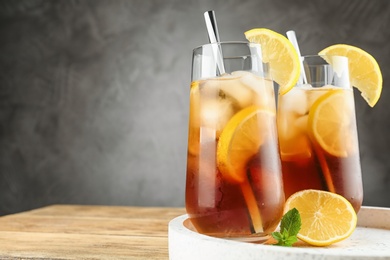 Glasses of refreshing iced tea on wooden table against grey background. Space for text
