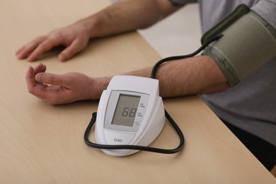 Photo of man checking blood pressure at wooden table indoors, closeup